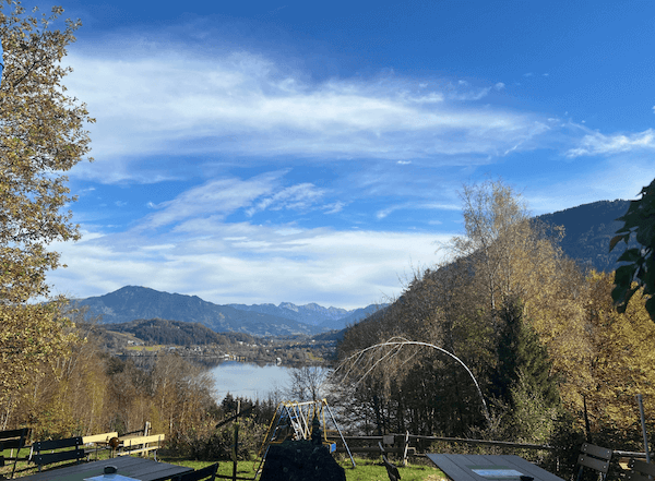 Herbstlicher Blick über bunte Bäume auf den Alpsee und die Allgäuer Berge unter blauem Himmel